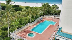 Ett poolområde med två pooler, omgivet av palmer och med utsikt över stranden.