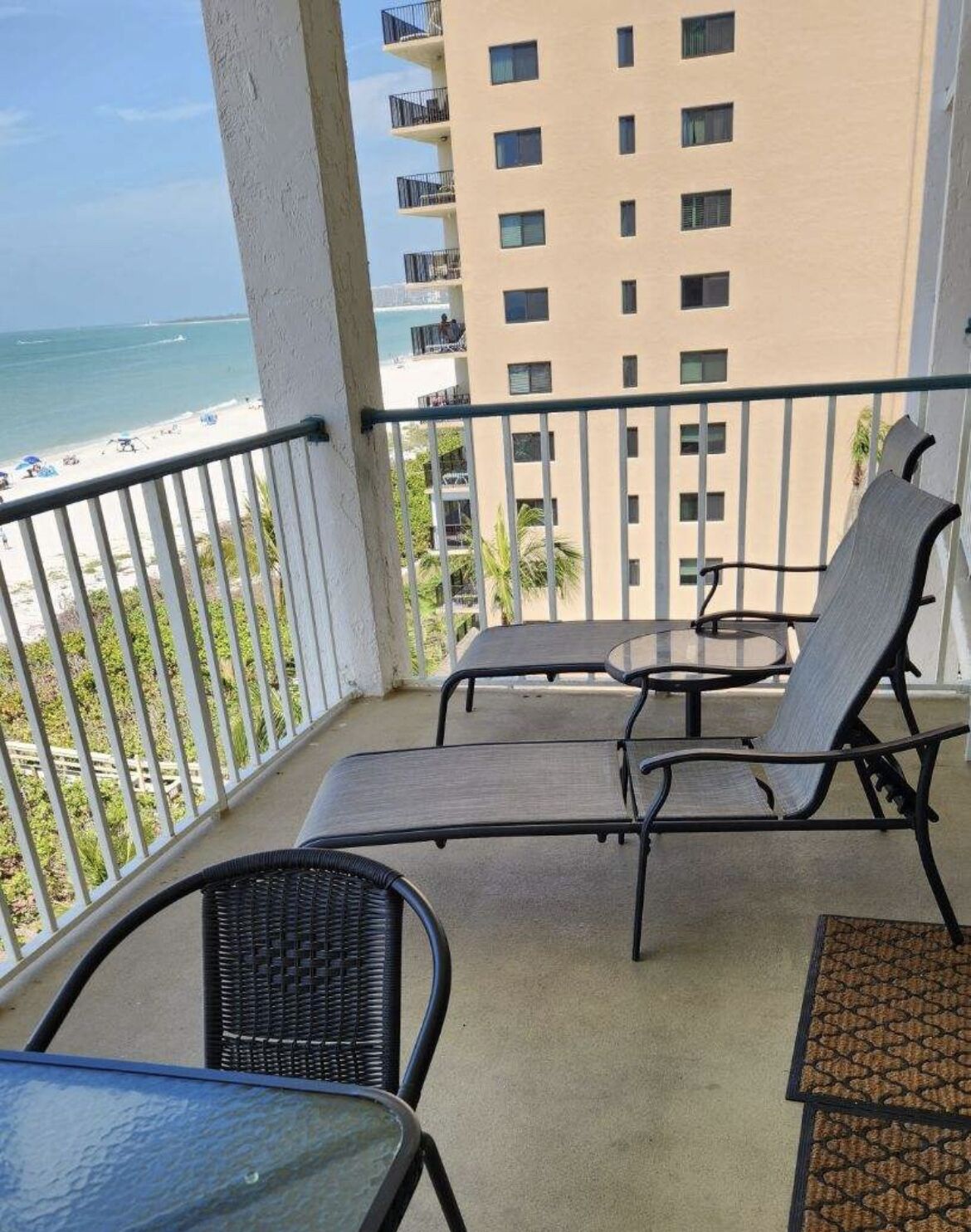 A balcony with a table and two chairs, overlooking a beach and ocean.