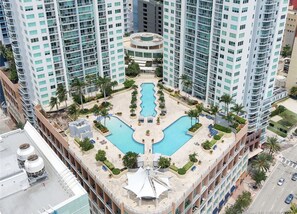 A high-rise hotel with a central swimming pool, multiple balconies, and surrounding greenery. - Resort style with pool and water views  (Miami)