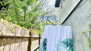 A wooden fence with a white curtain featuring a tropical leaf pattern. - Private unique home short 5 minutes walk to the beach and the bay. (Hull)