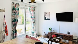 A living room with a wooden dining table, a TV mounted on the wall, and a ceiling fan. - Private unique home short 5 minutes walk to the beach and the bay. (Hull)