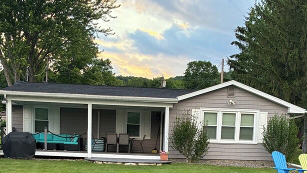 A house with a covered porch, a lawn, and a body of water. - Spring Summer specials on cozy newly renovated cottage with AC right on the lake (Honeoye)