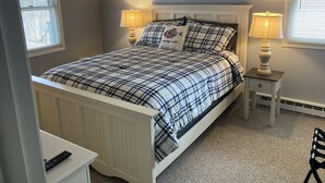 A bedroom with a bed, two bedside lamps, a nightstand, a remote control, and a picture on the wall. - Spring Summer specials on cozy newly renovated cottage with AC right on the lake (Honeoye)