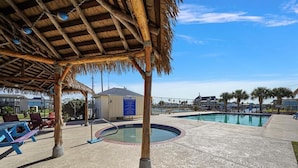 A pool area with a thatched-roof pavilion, lounge chairs, and a small building with a sign. - Awesome Bay View Home with Two Living Areas!  Pets welcome! (Galveston)