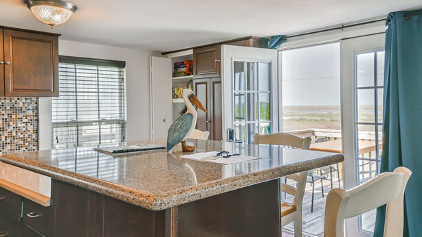 A kitchen with a granite countertop, a wooden cabinet, and a view of the beach through a large sliding glass door. - Awesome Bay View Home with Two Living Areas!  Pets welcome! (Galveston)