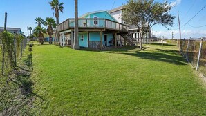 A two-story house with a balcony, surrounded by a well-maintained lawn and palm trees. - Awesome Bay View Home with Two Living Areas!  Pets welcome! (Galveston)