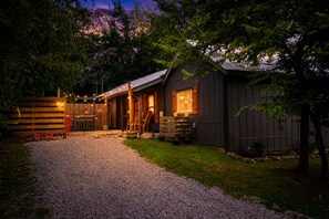 A rustic cabin with a gravel driveway leading to a wooden deck, surrounded by trees and a wooden fence. - Walkable Pigeon Forge Escape + Hot Tub (Pigeon Forge)