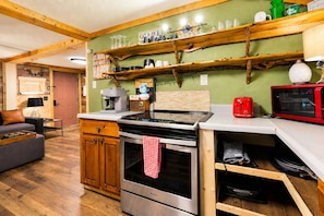 Una cucina compatta con piano cottura, forno e microonde. Ripiani in legno sopra il bancone contengono diversi utensili da cucina.