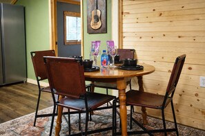 Une table à manger en bois avec quatre chaises, un tapis à motifs, une décoration murale représentant une guitare et un réfrigérateur, le tout dans une pièce aux murs verts et aux panneaux de bois.