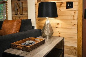 Une pièce chaleureuse avec un mur en bois, une lampe noire, un canapé et une petite table en bois agrémentée d’un objet décoratif.
