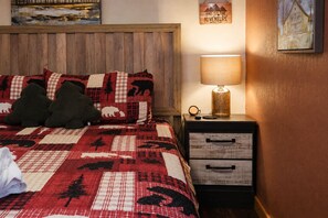 A hotel room with a wooden headboard, a quilted bedspread with animal prints, a bedside lamp, and a nightstand with drawers.