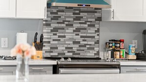 Una cocina moderna con campana de acero inoxidable, salpicadero azulejado y diversos utensilios y electrodomésticos.