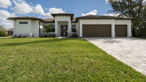 A modern two-story house with a garage, a well-maintained lawn, and a clear sky. - Beautiful modern pool home; Furnished lanai, gas grill; Free Wifi; Nearby park (Cape Coral)
