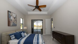 A bedroom with a bed, a dresser, a ceiling fan, a door, and a window. - Beautiful modern pool home; Furnished lanai, gas grill; Free Wifi; Nearby park (Cape Coral)