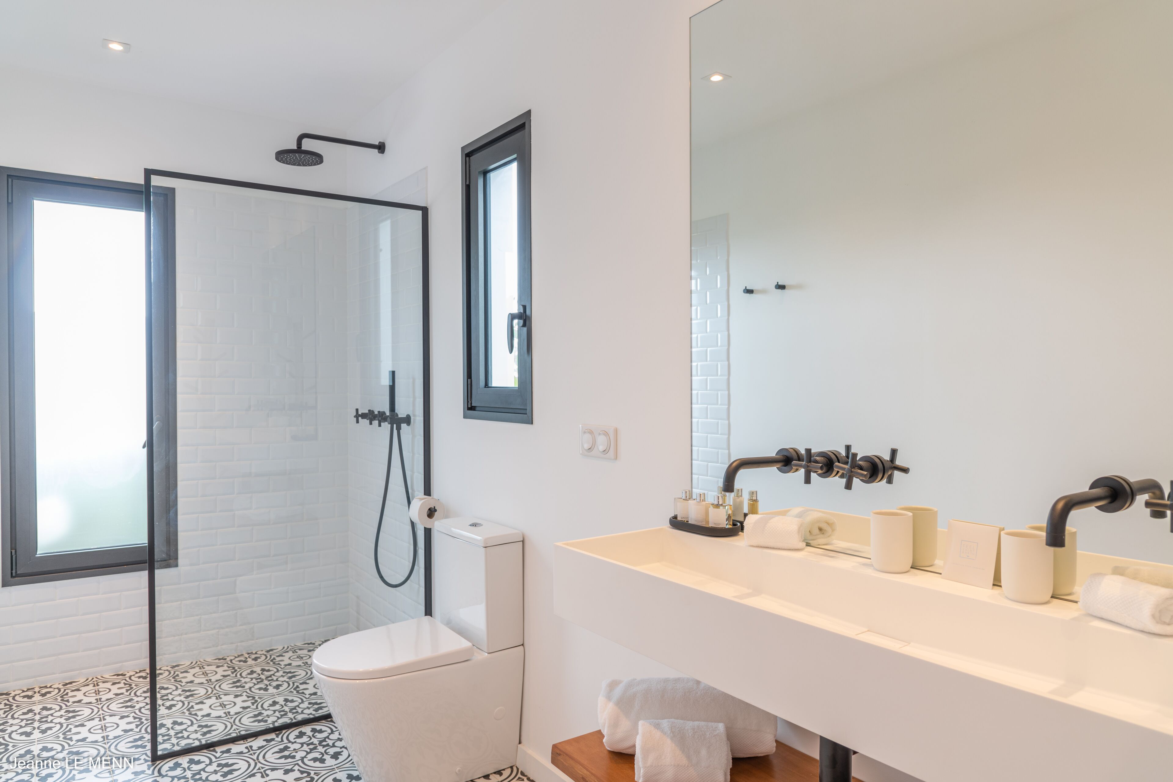 A modern bathroom with a glass shower enclosure, a white toilet, a large mirror, and a white sink with toiletries.