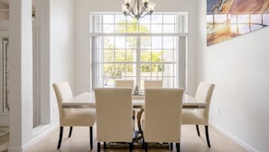A dining room with a large window, a chandelier, and a painting on the wall. - Entire home with pool for long and short stay. Fun for everyone.  (Port St. Lucie)