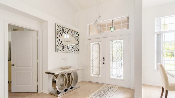 A spacious entryway with a white door, a decorative mirror, and a console table. - Entire home with pool for long and short stay. Fun for everyone.  (Port St. Lucie)