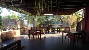 An outdoor patio with wooden tables and chairs, surrounded by potted plants and a bamboo fence.