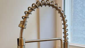 Una cocina con un lavamanos de acero inoxidable, un grifo moderno con manguera flexible y una ventana con vistas al exterior.