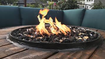 Un pozo de fuego circular de carbón con llamas sobre una mesa de madera, rodeado de asientos verdes para exteriores.
