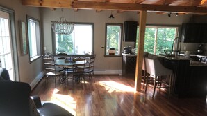 A spacious room with a wooden floor, a dining table with chairs, a bar area, and large windows allowing natural light.