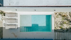 A rooftop pool with a clear blue water feature, surrounded by a white wall and a small garden area with plants.