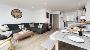 Un salon moderne avec un canapé d’angle gris, une table basse en bois et un coin repas aménagé pour un repas.