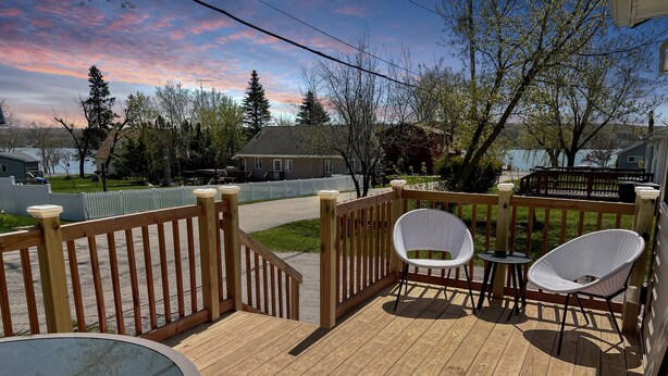A wooden deck with two white wicker chairs and a small table, a glass-top table, and a striped rug. - Escape to the Lake! Walk to water & local dining! (Lake Geneva)