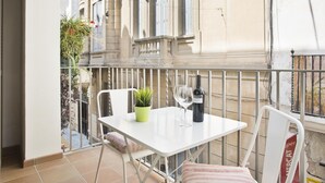 Ein kleiner Balkon mit einem weißen Tisch, zwei Stühlen, einem Blumentopf und einer Weinflasche.