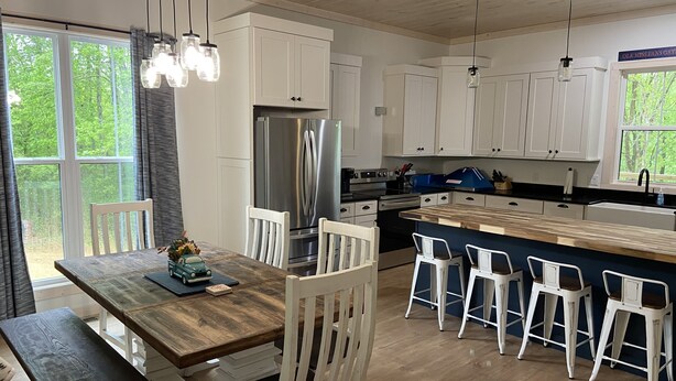 Een moderne keuken met witte kasten, roestvrijstalen apparatuur en een houten eettafel met witte stoelen.
