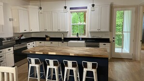 Een moderne keuken met witte kasten, een houten kookeiland met barstoelen, en een raam met uitzicht op groen.