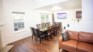 A dining area with a wooden table and chairs, a brown leather couch, and a television mounted on the wall.