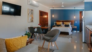 A modern hotel room with a flat-screen TV, a dining area with chairs and a table, a bed with a wooden headboard, and a kitchenette. - Mare Lindo open studio near Malecon Progreso (Progreso)