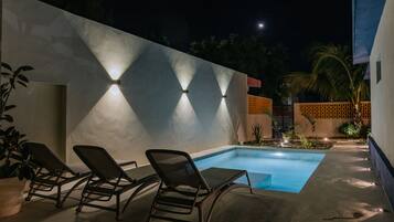 A swimming pool area with lounge chairs and wall-mounted lights.