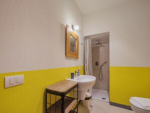 A bathroom with a yellow and white color scheme, a wooden bench, a sink, a mirror, and a shower.