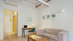 En moderne stue med et træbord, en beige sofa, et skrivebord med en bærbar computer og tre billeder hængende på væggen.