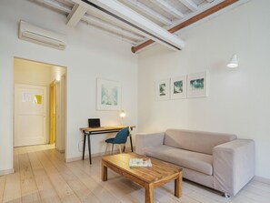 A modern living room with a wooden coffee table, a beige sofa, a desk with a laptop, and framed artwork on the wall.