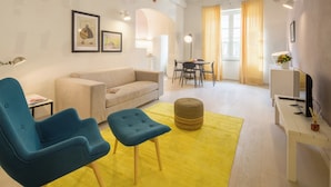 En moderne stue med sofa, blå lænestol, skammel og et spiseområde med bord og stole.