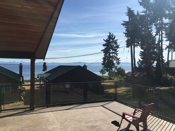 A balcony with a view of a body of water and mountains. There are chairs and a table on the balcony.