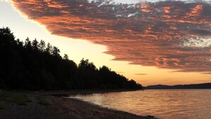 Auringonlasku tyynen järven yllä, jonka rannalla kasvaa metsä.