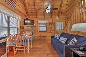 A wooden cabin interior with a dining area, a sofa, and a ceiling fan.
