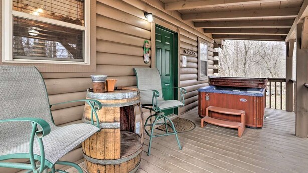 A covered porch with a wooden barrel, a green door, and a hot tub. - Cozy `American Dream` Cabin w/ Hot Tub, Loft & BBQ!!! (Cosby)
