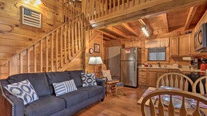 A wooden cabin interior with a sofa, dining table, chairs, a kitchen area, and a staircase. - Cozy `American Dream` Cabin w/ Hot Tub, Loft & BBQ!!! (Cosby)