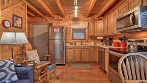 A wooden cabin interior with a kitchenette, a dining area with a table and chairs, and a living area with a sofa and a lamp. - Cozy `American Dream` Cabin w/ Hot Tub, Loft & BBQ!!! (Cosby)
