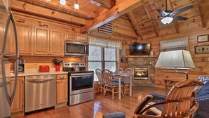 A cozy cabin-style interior with wooden walls and ceiling, a dining area with chairs, a fireplace, and modern appliances like a microwave and oven. - Cozy `American Dream` Cabin w/ Hot Tub, Loft & BBQ!!! (Cosby)