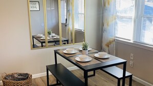 A dining area with a table set for four, a bench, a mirror, and a window with blinds. - Secret Hideaway (Rossville)