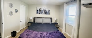A bedroom with a bed, two bedside tables, a cityscape painting, and a window with blinds. - Secret Hideaway (Rossville)