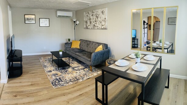 A modern living room with a grey sofa, yellow cushions, a black coffee table, and a dining table set for four. - Secret Hideaway (Rossville)