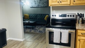 A kitchen with wooden cabinets, a stainless steel stove, and a dining area with a sofa and a rug. - Secret Hideaway (Rossville)