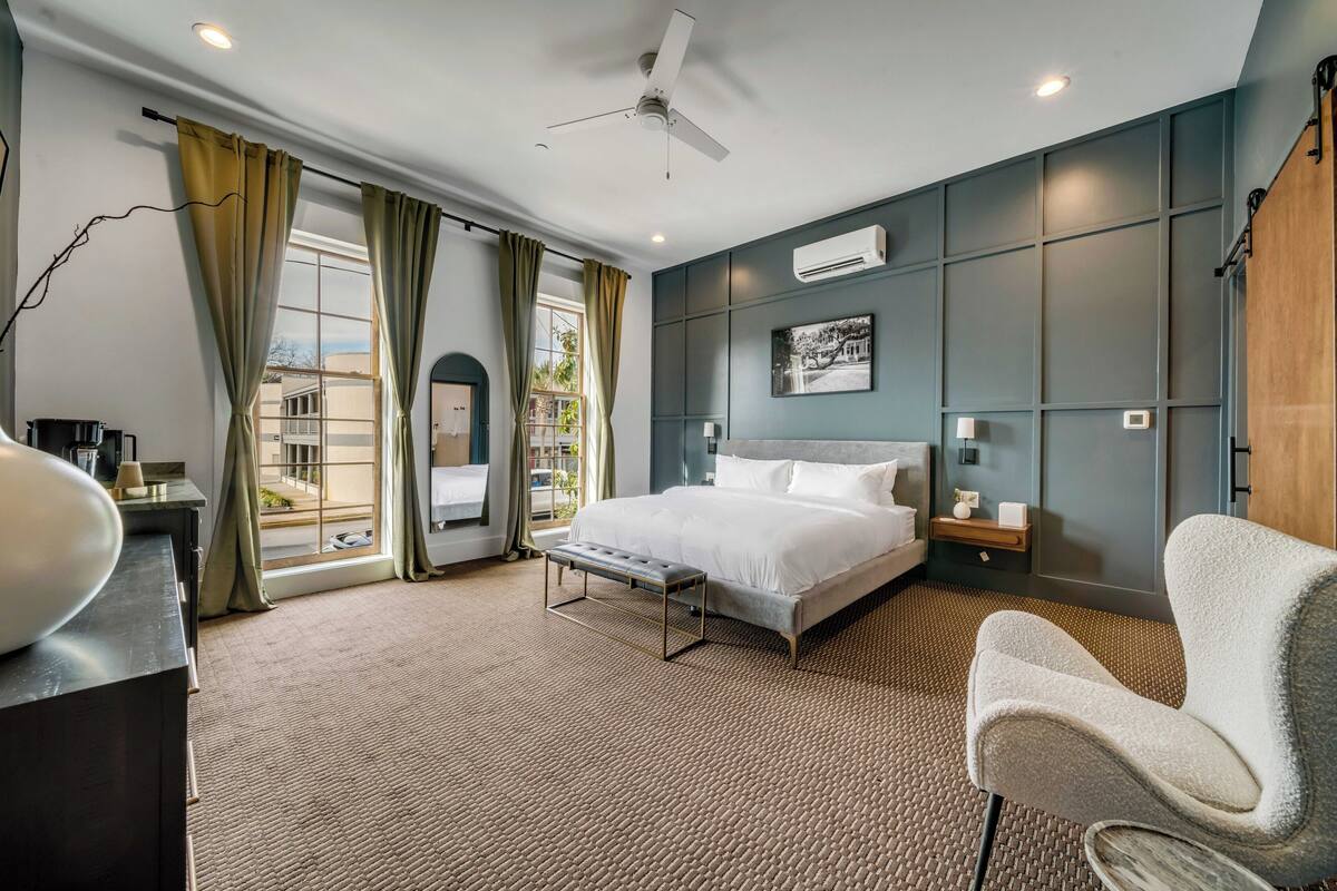 A bedroom with a bed, a chair, a desk, and a view of the outdoors.